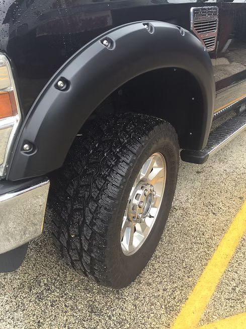 Black truck tire and fender. Chrome wheel. Wet, dark tire.