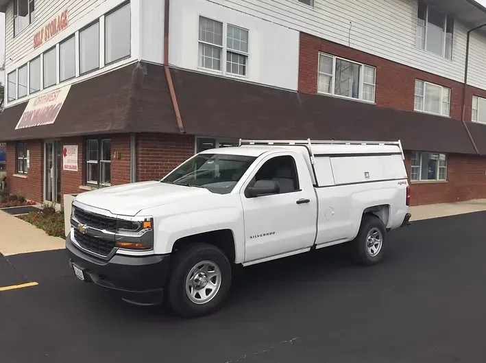White pickup truck with a utility topper parked in front of a brick building.
