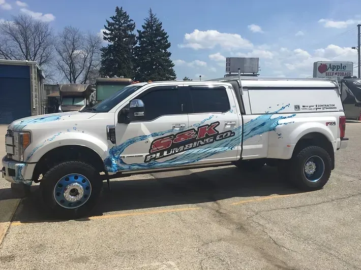 White truck with blue water splash design and company logo parked outside.