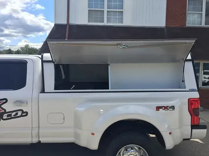 White pickup truck with a silver utility cap, open to reveal storage.