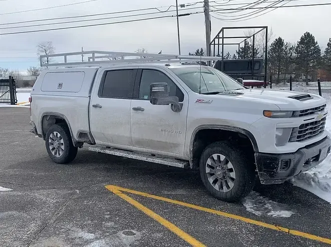 White Chevrolet truck with cap and roof rack parked in snowy area.