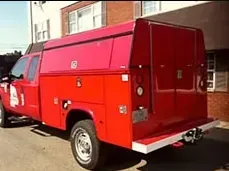 Red service truck with a utility body, parked outdoors.