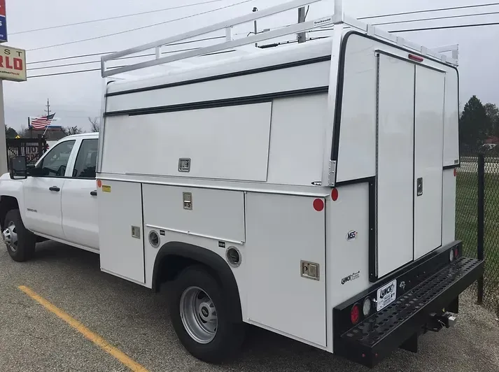 White work truck with utility body and roof rack parked outdoors.