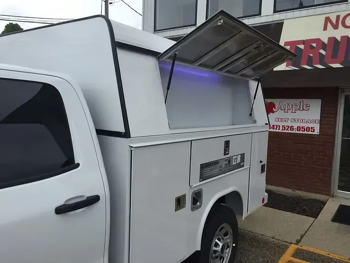 White truck with utility bed, open top, side compartments.  Blue interior lighting visible.