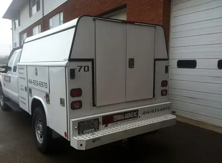White work truck with enclosed back and rear doors, parked near a building.