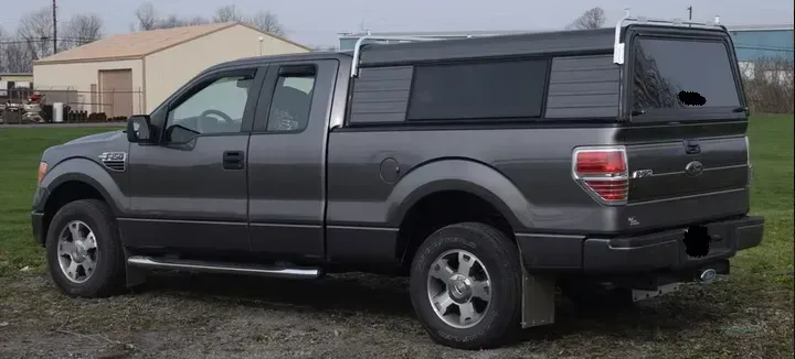Gray Ford F-150 pickup truck with a camper shell parked on gravel.