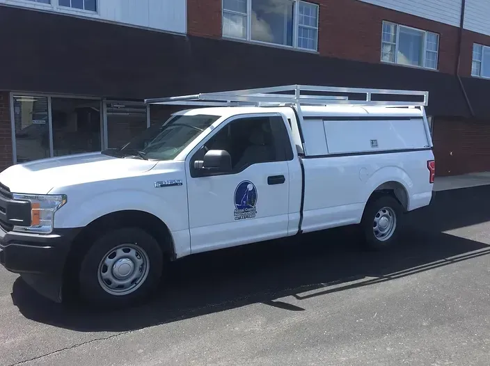 White pickup truck with a cap and roof rack parked in front of a building.