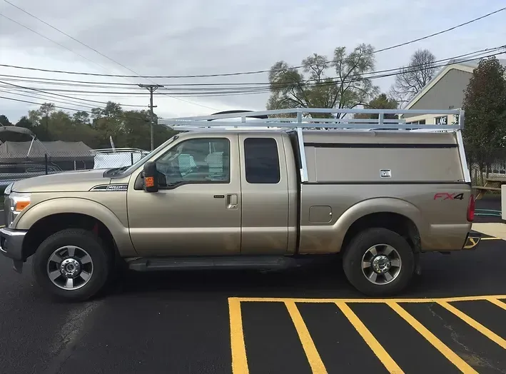 Gold Ford pickup truck with a camper shell and roof rack parked outdoors.