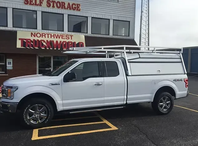 White pickup truck with a cap and ladder rack parked in front of a Northwest Truckworld building.