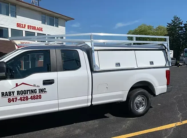White pickup truck with tool boxes and roof rack, parked outside a self-storage facility.