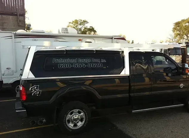 Black truck with a silver utility cap and roof rack, parked next to a white RV.