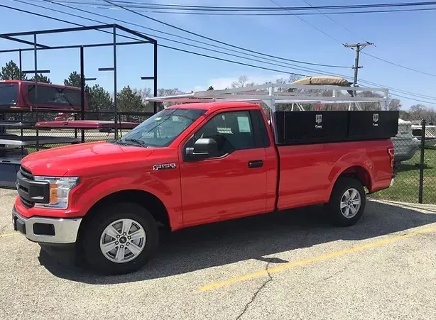 Red Ford F-150 truck with black storage compartments and a silver roof rack, parked outdoors on a sunny day.
