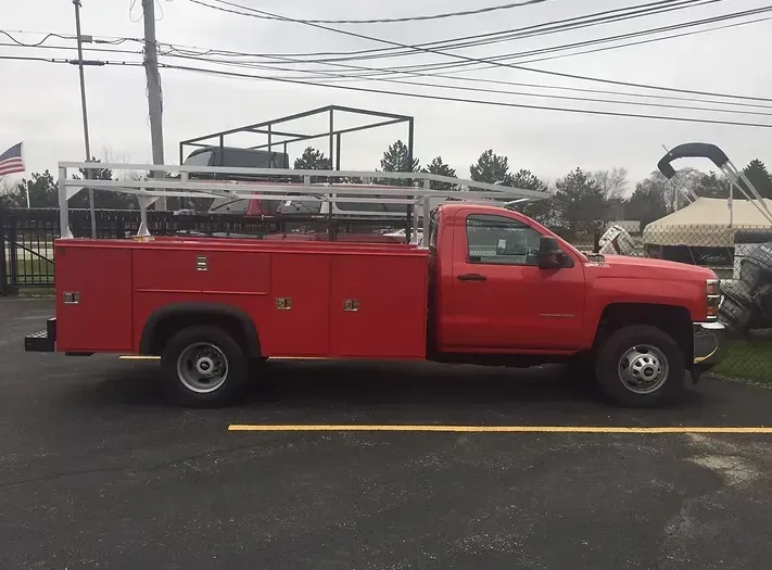 Red work truck with a storage bed and roof rack parked on asphalt.