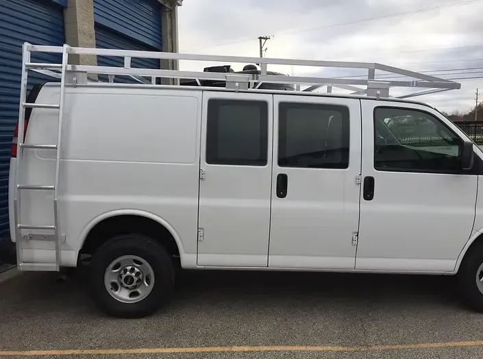 White cargo van with ladder rack on roof and side ladder.