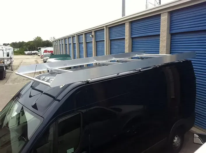 Dark blue van with a silver roof rack in front of blue storage units.
