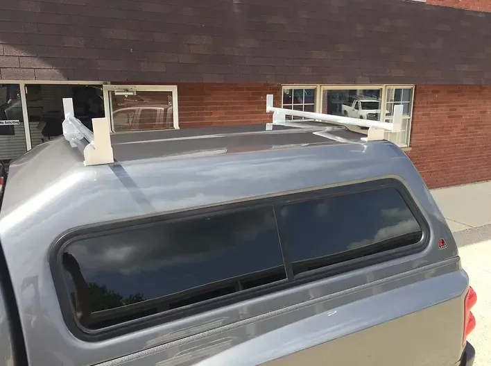 Gray pickup truck bed with a white ladder rack on top.