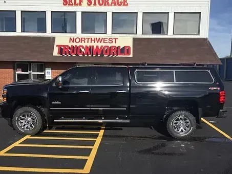 Black pickup truck with a camper shell parked in front of Northwest Truckworld building.