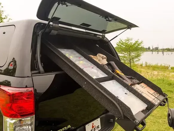 Black truck bed with pull-out storage compartments, holding various items, with open rear window.