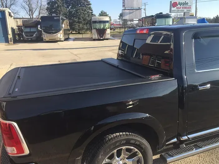 Black pickup truck with a closed tonneau cover, parked outside with buses in the background.