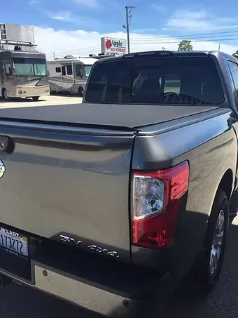 Gray Nissan Titan pickup truck with closed black bed cover, parked outside, sunny day.