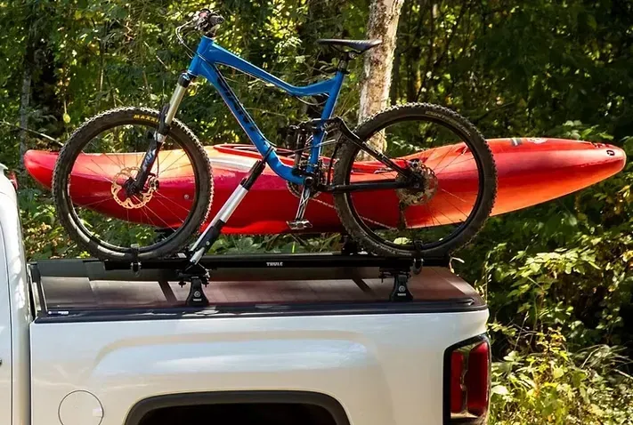 White pickup truck with blue mountain bike and red kayak mounted on the bed.