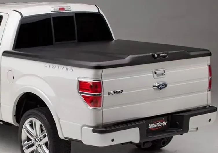 White Ford F-150 truck with a black tonneau cover over the bed. Rear view, parked in a studio setting.