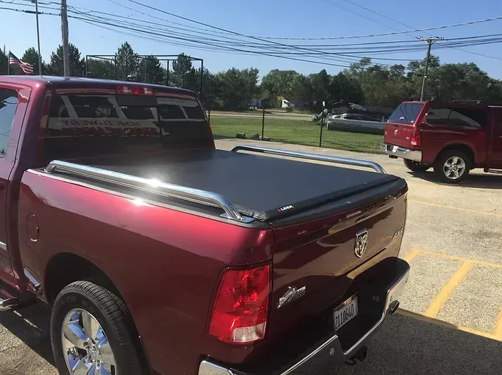 Red pickup truck with a black tonneau cover and chrome bars, parked in a lot on a sunny day.