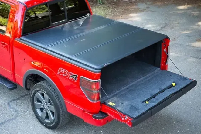Red pickup truck with a black, folded bed cover; tailgate is open.