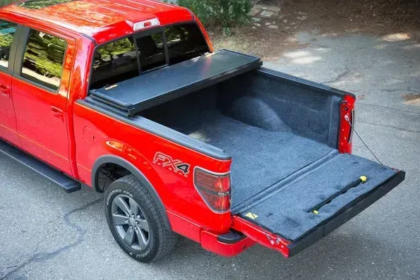 Red pickup truck with a black tonneau cover and open tailgate.
