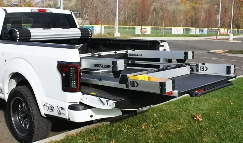 White pickup truck with a sliding cargo bed extended on grass.