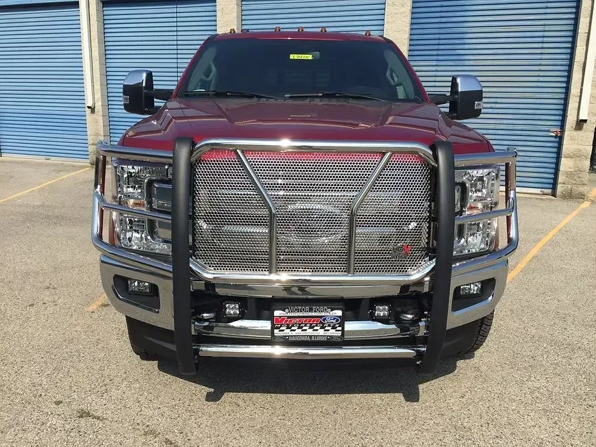 Red pickup truck with a large, chrome grill guard parked in front of blue storage doors.