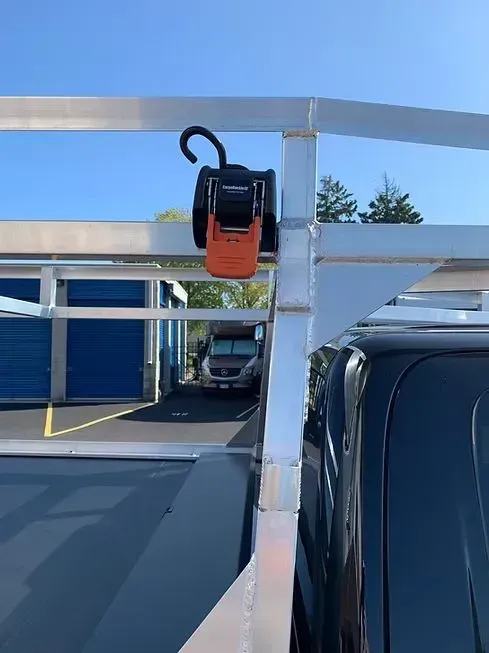 Orange and black ratchet strap mounted on a metal truck rack, truck bed visible.