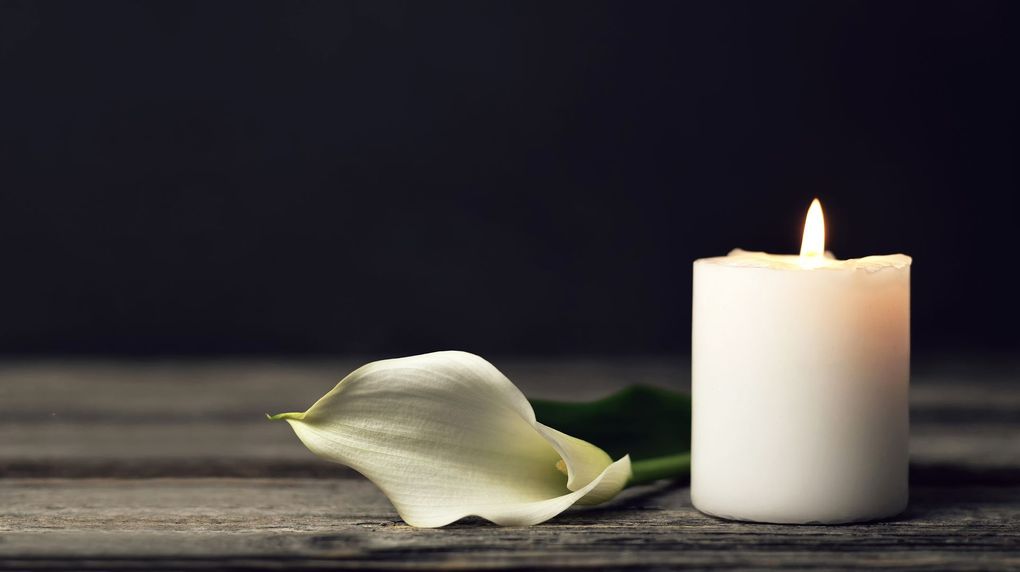 White candle burning beside a pale flower on a dark surface