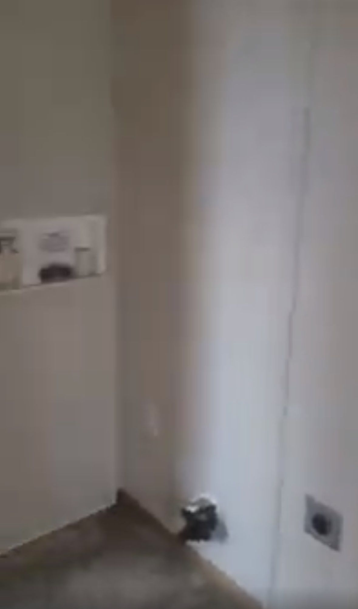 Empty corner laundry room with utility connections on the wall and a small shelf on the adjacent wall.