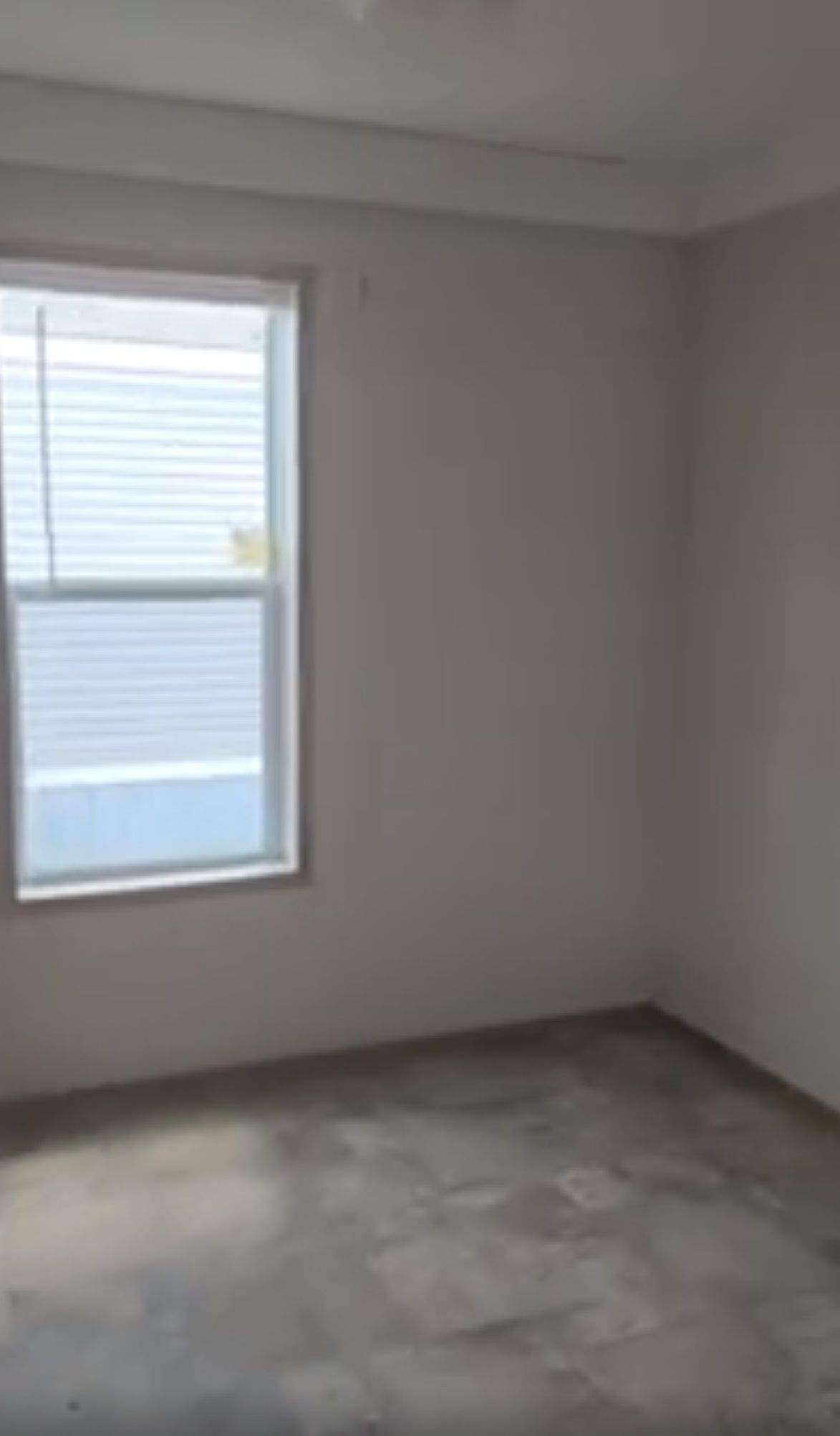 Empty room with window, blinds, and grey carpet. White walls and ceiling.