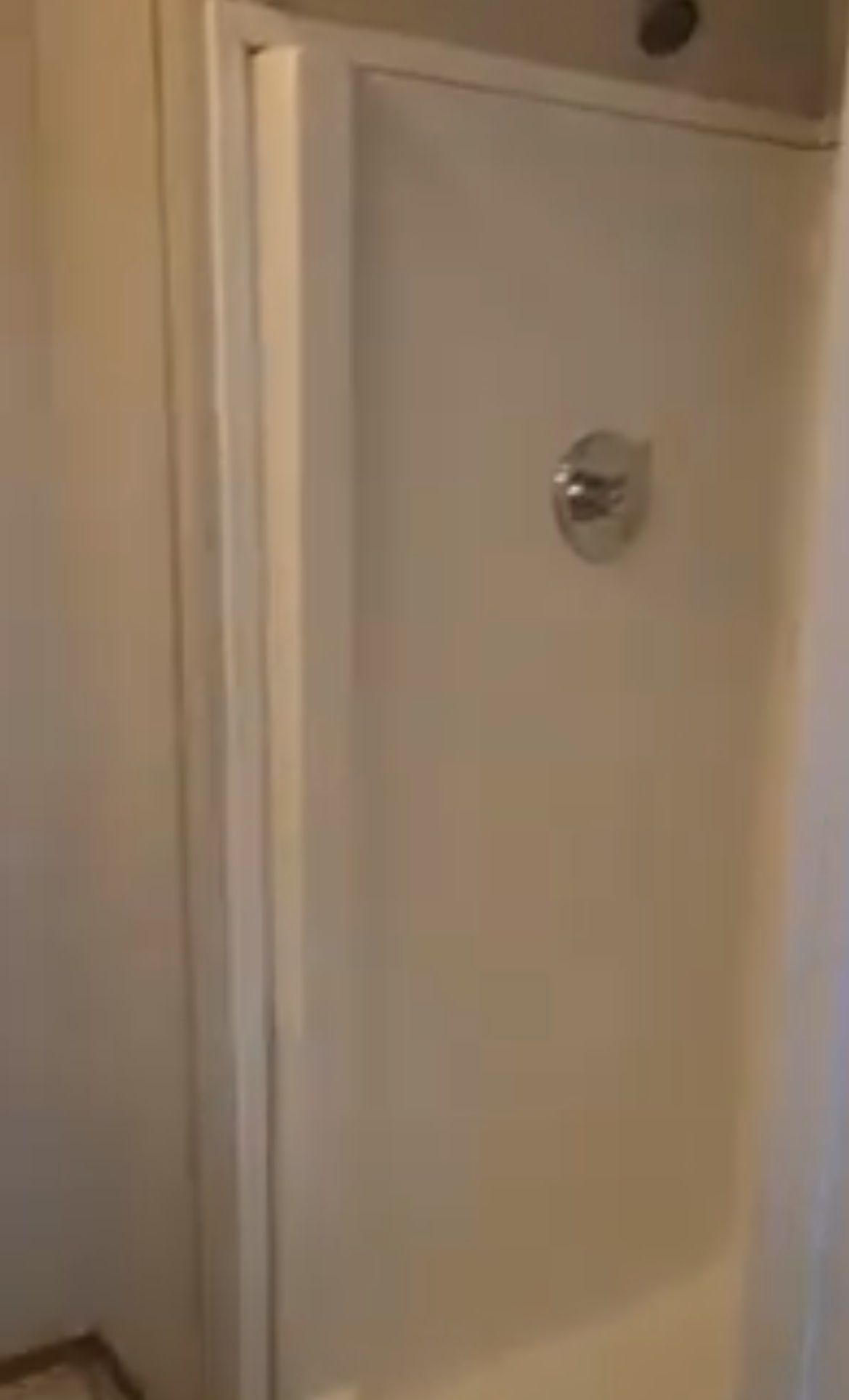 White shower stall with a single faucet and a showerhead.