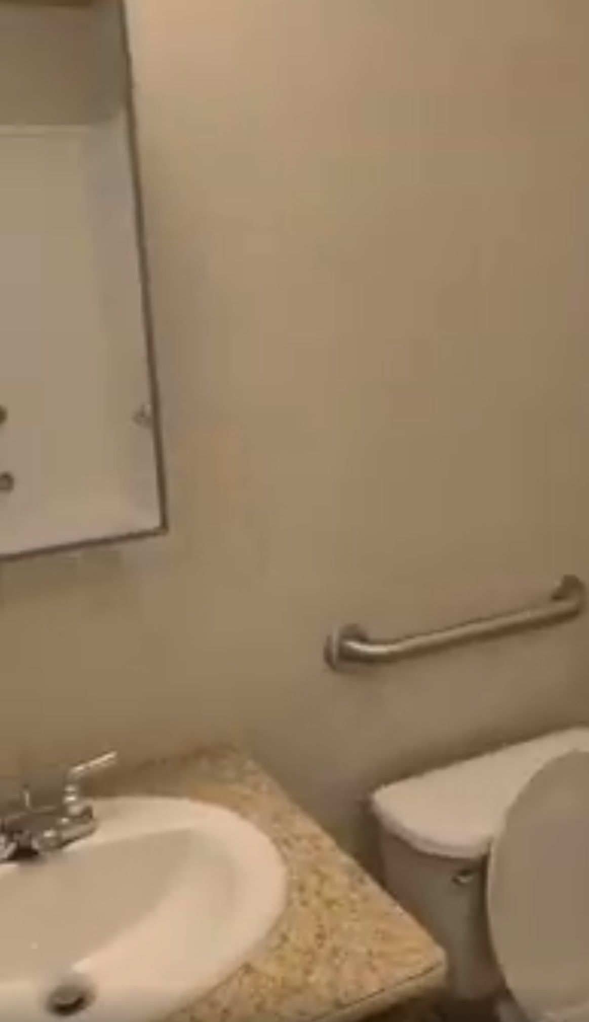 Bathroom with a sink, mirror, toilet with a grab bar, and light-colored walls.