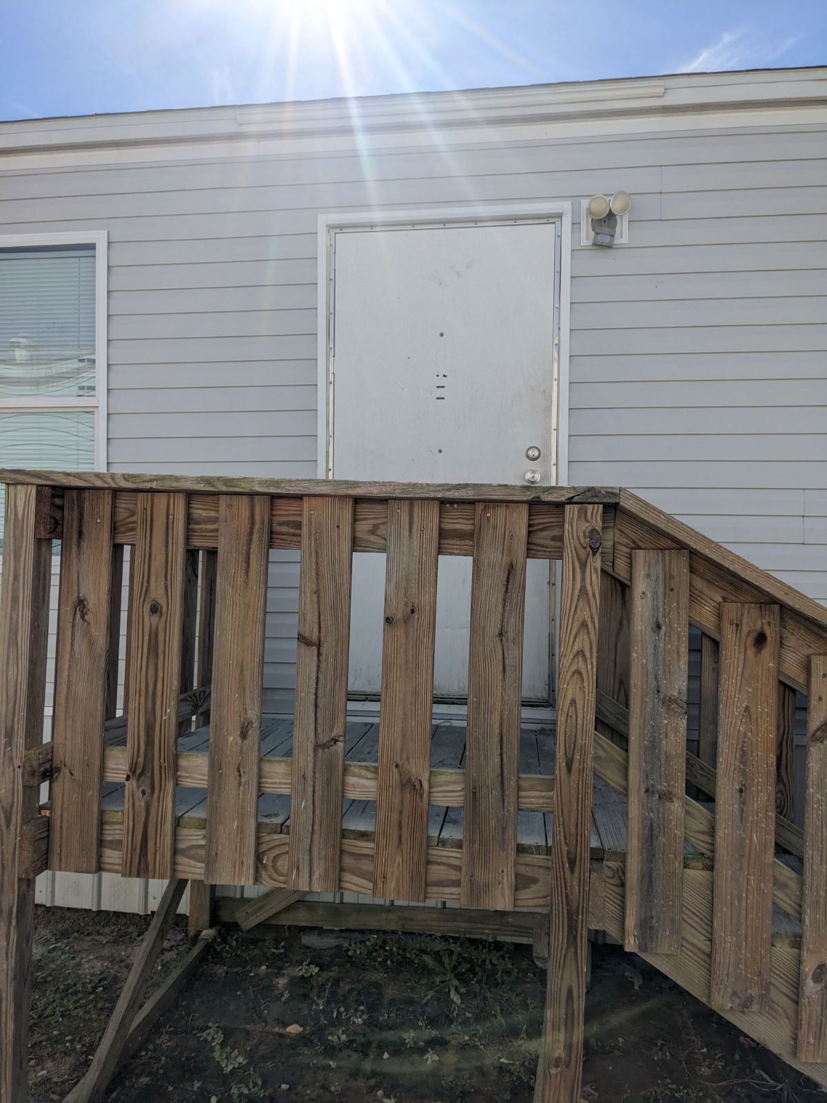 Wooden stairs leading to a white door on a light gray house. Bright sunlight.