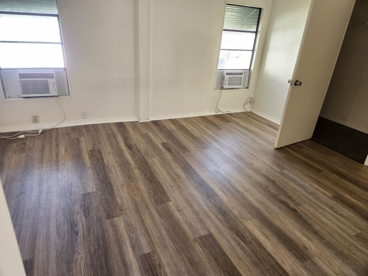 Empty room with wood-look flooring, two windows with AC units, and a closet door.