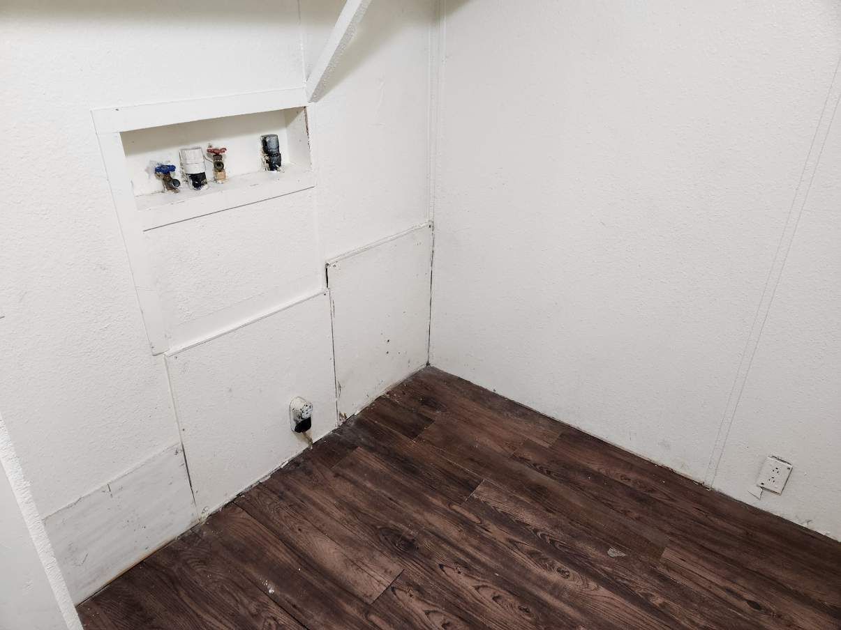 Laundry room with white walls, wood-look flooring, and a shelf. Plumbing hookups visible.