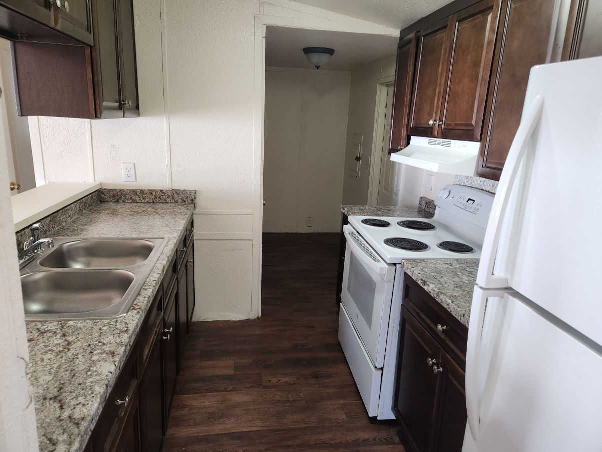 Kitchen with dark cabinets, white appliances, granite countertops, and dark flooring.