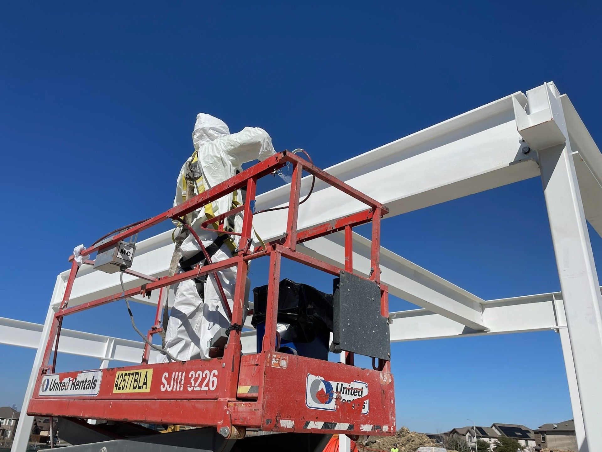 A man wearing a protective suit is standing on a scissor lift.