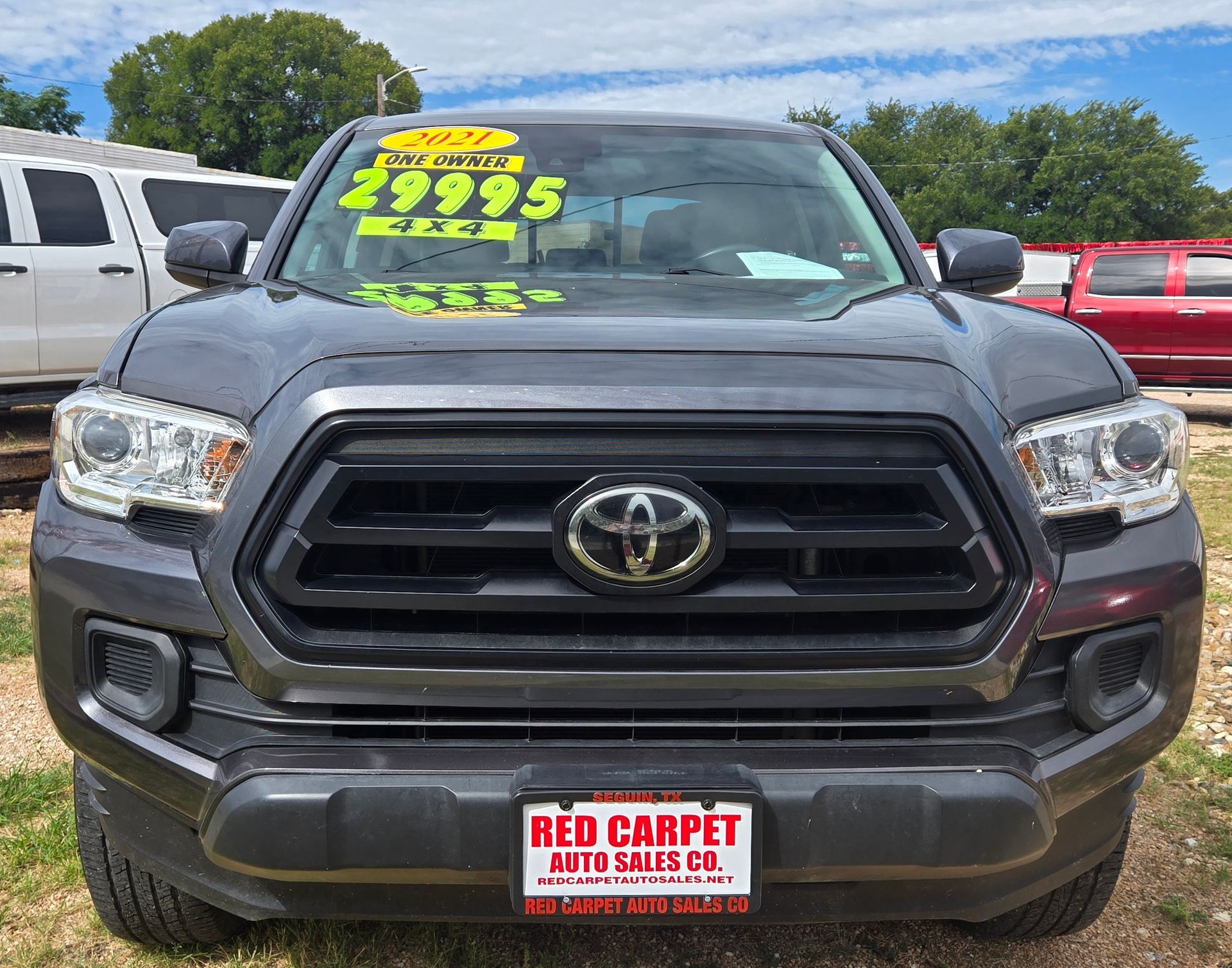 A gray Toyota Tacoma truck with a black grille on display at Red Carpet Auto Sales. It has a price tag of $29,995.
