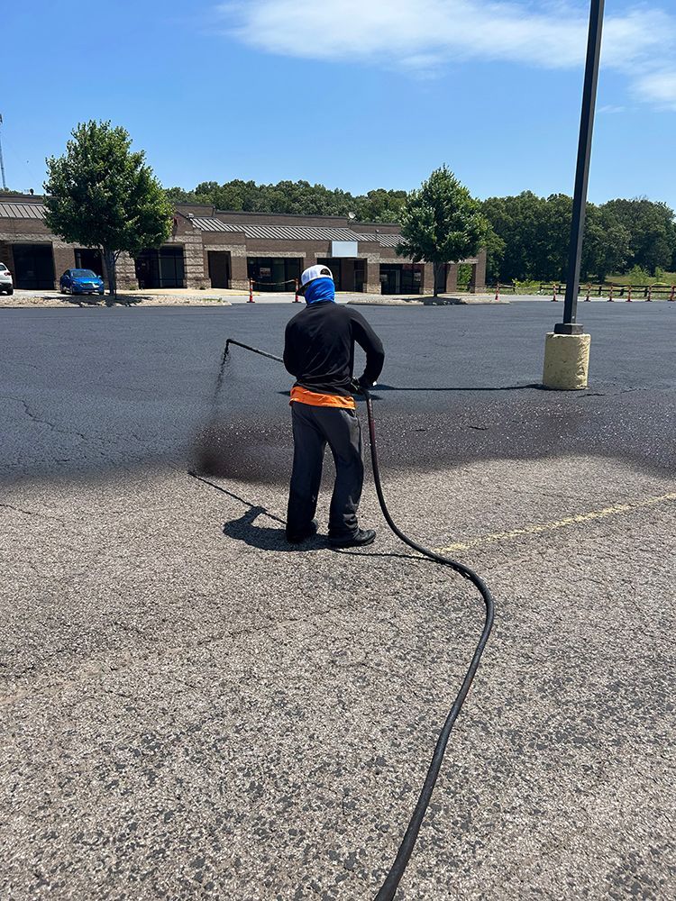 A man is spraying asphalt in a parking lot.
