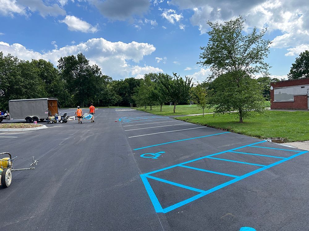 A group of people are painting blue lines on a parking lot.
