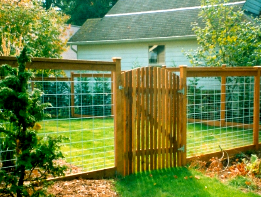 Wooden fence with gate in a yard, with wire mesh sections, green grass, and a house in the background.