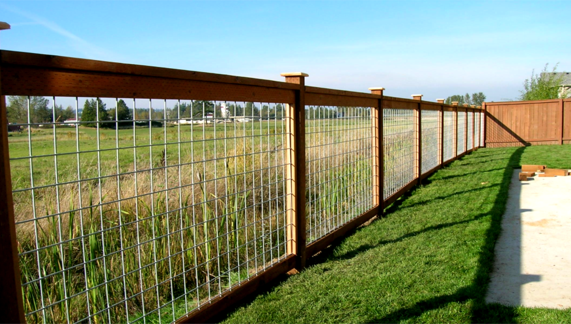 Wooden fence with wire mesh panels, green grass, and a clear blue sky.