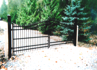Black iron gate with arch design, set between two dark wooden posts; gravel driveway.
