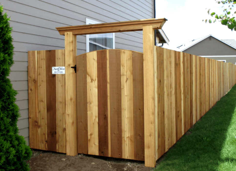 Wooden fence with gate in a residential backyard; the gate features a decorative top and a sign.