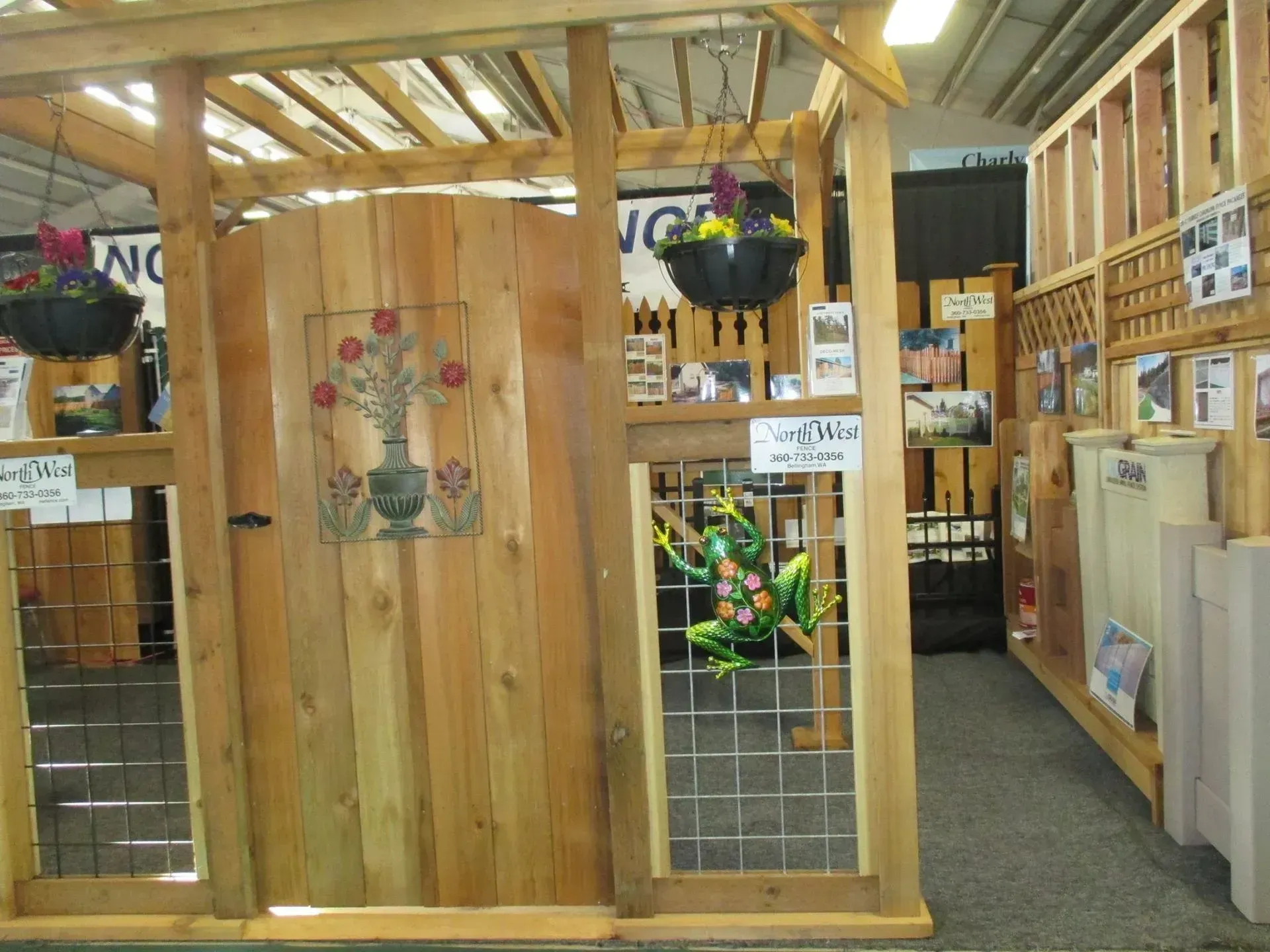 Wooden garden gate display with hanging baskets, decorative glass insert, and frog statue.